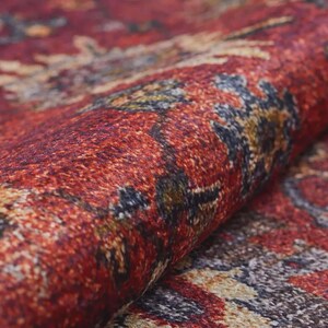 K&ouml;nnte beinhalten: Nahaufnahme eines aufgerollten Teppichs mit komplexem Muster. Der Teppich zeigt Farbt&ouml;ne von Rot, Braun, Gold und Blau. Die Textur ist weich und detailliert, mit sichtbaren gewebten F&auml;den.