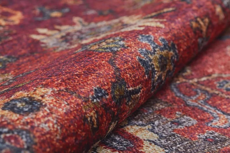 K&ouml;nnte beinhalten: Nahaufnahme eines aufgerollten Teppichs mit komplexem Muster. Der Teppich zeigt Farbt&ouml;ne von Rot, Braun, Gold und Blau. Die Textur ist weich und detailliert, mit sichtbaren gewebten F&auml;den.