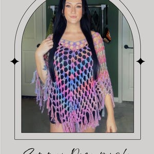 以下が含まれることがあります： ピンク、青、紫の色合いの、フリンジ付きのカラフルなかぎ針編みポンチョ。 オープン織りのデザインが見え、画像の下部には「Summer Daze poncho」というテキストがスクリプトで書かれています。 ポンチョは夏の衣服です。