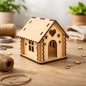 Puede incluir: Una pequeña casa de madera sin terminar, con un recorte en forma de corazón y estrellas. El tejado tiene un borde festoneado, y la casa presenta una ventana y una puerta arqueada. Hecha de madera clara con bordes más oscuros.