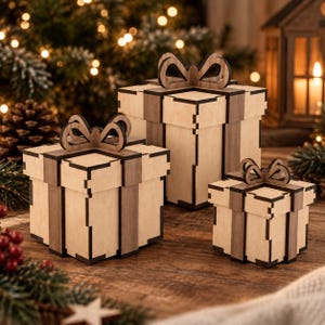 May include: Three square gift boxes constructed from light-coloured wood with darker wood accents forming ribbons and bows on top. The boxes feature visible interlocking joints at the corners and edges, showcasing a layered, geometric construction.