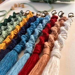 Puede incluir: Un conjunto de nueve llaveros de macramé de colores con borlas. Los llaveros están hechos con una variedad de colores, incluyendo verde, amarillo, azul, rojo y blanco. Cada llavero tiene un cierre de metal dorado.