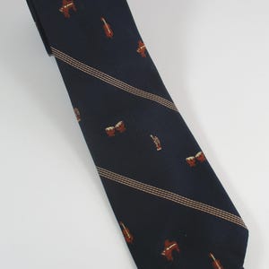 May include: A dark navy blue necktie featuring a repeating pattern of small musical instruments including violins, drums, and trumpets, accented by thin, diagonal, light-colored pinstripes running across the length of the fabric.