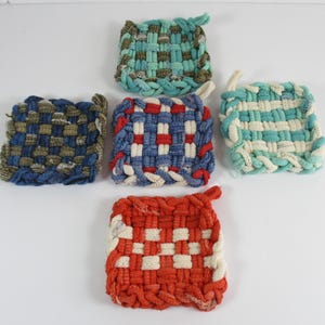 May include: Five colorful, square woven pot holders in shades of blue, green, red, and white. Each pot holder has a loop for hanging. The woven design creates a textured appearance. These are ideal for kitchen use.