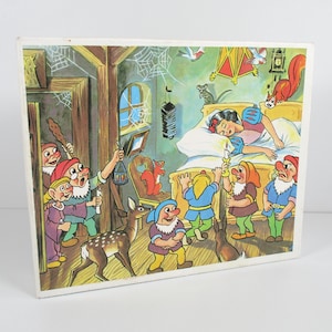 May include: A rectangular wooden puzzle board featuring a colorful illustration of Snow White sleeping in a bed surrounded by seven dwarfs, a deer, a squirrel, and a mouse. The scene is set in a rustic room with wooden beams, spiderwebs, and a lantern.