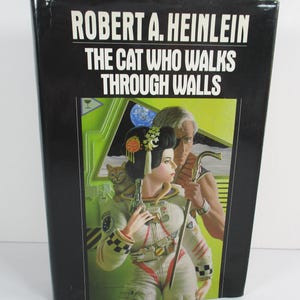 May include: A hardcover book titled "THE CAT WHO WALKS THROUGH WALLS" by Robert A. Heinlein. The cover features a woman in a spacesuit, a cat, and a man with a cane, set against a space-themed backdrop.