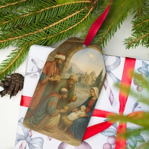 May include: A Christmas gift tag with a religious illustration of the Nativity scene, featuring the Three Wise Men, Mary, and baby Jesus. The tag is attached to a wrapped gift with a red ribbon, and is surrounded by pine branches.