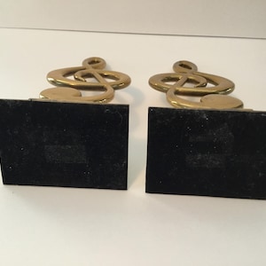以下が含まれることがあります： 2つの金色の金属製ト音記号ブックエンド。各ブックエンドは黒い長方形のベースを持っています。ト音記号のデザインはクラシックな音楽記号であり、音楽愛好家にとって装飾的なアイテムとなっています。