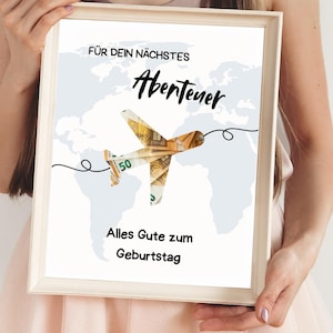 May include: A framed print featuring a world map background with a stylized airplane made of Euro banknotes. The text reads "FÜR DEIN NÄCHSTES Abenteuer Alles Gute zum Geburtstag" in black font. The frame is a light wood color.