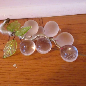 May include: A glass grape cluster with frosted and clear glass grapes, with green leaves and a wire stem.