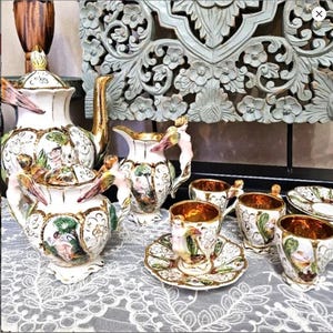 Puede incluir: Un juego de té de porcelana italiana vintage con un delicado diseño floral y detalles dorados. El juego incluye una tetera, una jarra de crema, un azucarero y cuatro tazas y platillos.