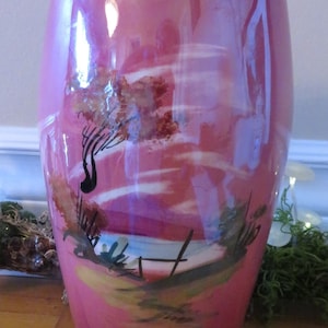 以下が含まれることがあります： 金色の縁取りと、絵付けされた風景画が施されたピンク色の陶器の花瓶。花瓶は丸みを帯びた楕円形で、光沢のある仕上げです。