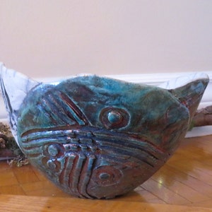 May include: A ceramic bowl with a teal, blue, and copper glaze. The bowl has a unique, organic shape and features a decorative design.