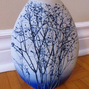 Puede incluir: Un jarrón de cerámica blanca con un esmalte azul y un diseño de ramas y hojas.