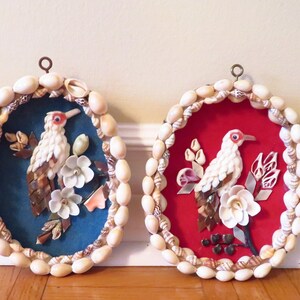 Puede incluir: Dos colgantes de pared redondos hechos de conchas marinas. Cada uno presenta un pájaro blanco con un pico rojo y un diseño floral. Uno tiene un fondo azul y el otro un fondo rojo.