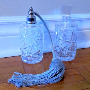 Peut inclure: Deux flacons de parfum en verre transparent avec un motif en verre taillé et des bouchons argentés. Un flacon a un pompon bleu attaché au vaporisateur.