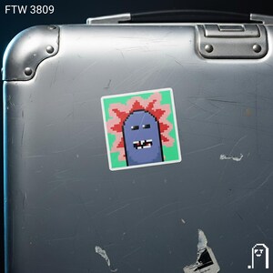 Puede incluir: Una pegatina cuadrada con una criatura azul pixelada con un dise&ntilde;o espinoso rojo y rosa sobre un fondo verde. La pegatina est&aacute; adherida a una maleta plateada. El texto "FTW 3809" est&aacute; en la esquina superior izquierda.
