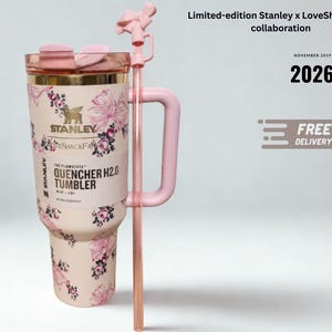 May include: A light pink Stanley x LoveShackFancy Quencher H2.0 tumbler featuring a floral and bow pattern, a gold-tone rim, a pink handle, and a matching straw with a bow topper. The label reads The Flowstate Quencher H2.0 Tumbler 40 oz 1.18 L.