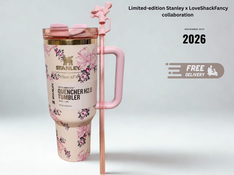 May include: A light pink Stanley x LoveShackFancy Quencher H2.0 tumbler featuring a floral and bow pattern, a gold-tone rim, a pink handle, and a matching straw with a bow topper. The label reads The Flowstate Quencher H2.0 Tumbler 40 oz 1.18 L.