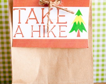 May include: A brown paper bag with a red and white tag that reads "TAKE A HIKE." The tag features a green and yellow tree graphic and is tied with twine. The background is a green and white checkered pattern.