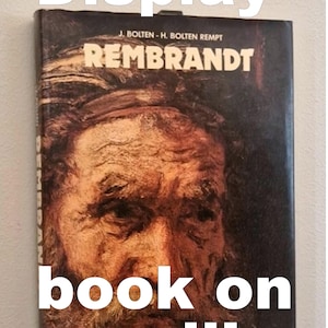 May include: A book titled "Rembrandt" displayed on a wall. The cover shows a portrait of a man against a dark backdrop. The words "Display book on wall!" are written on the image.
