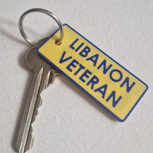 May include: A key with a silver metal key ring and a yellow rectangular tag. The tag has the words "LIBANON VETERAN" in blue text.