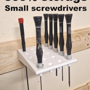 Pode incluir: Um suporte de armazenamento branco com várias pequenas chaves de fenda com cabos pretos e pontas prateadas. Uma chave de fenda tem um topo vermelho. O texto "500% storage Small screwdrivers" está no topo.