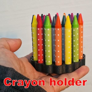 Könnte beinhalten: Ein Buntstifthalter mit einer Vielzahl von farbigen Buntstiften. Die Buntstifte sind kreisförmig angeordnet und mit weißen Punkten verziert. Der Text "Crayon holder" ist rot am unteren Rand des Bildes zu sehen.