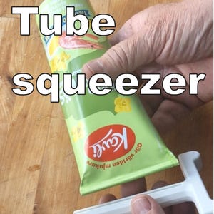 Könnte beinhalten: Eine grüne Tube des Lebensmittelprodukts der Marke Kavli mit rotem Deckel wird mit einem weißen Tubenquetscher ausgepresst. Die Tube hat eine Garnelen- und Zitronenillustration. Die Worte "Tube squeezer" sind in weißen Blockbuchstaben.