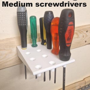 Peut inclure: Un support blanc pour tournevis avec plusieurs tournevis de différentes couleurs et tailles. Le texte "400% storage Medium screwdrivers" est affiché en haut. Le support est monté sur une surface en bois.