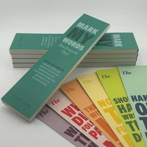 May include: A stack of green "Mark My Words" bookmark pads with colorful individual bookmarks fanned out. The pads have text that reads "Writable Bookmark Pad for notes, quotes, and thoughts..." and the brand name "Lorelium".