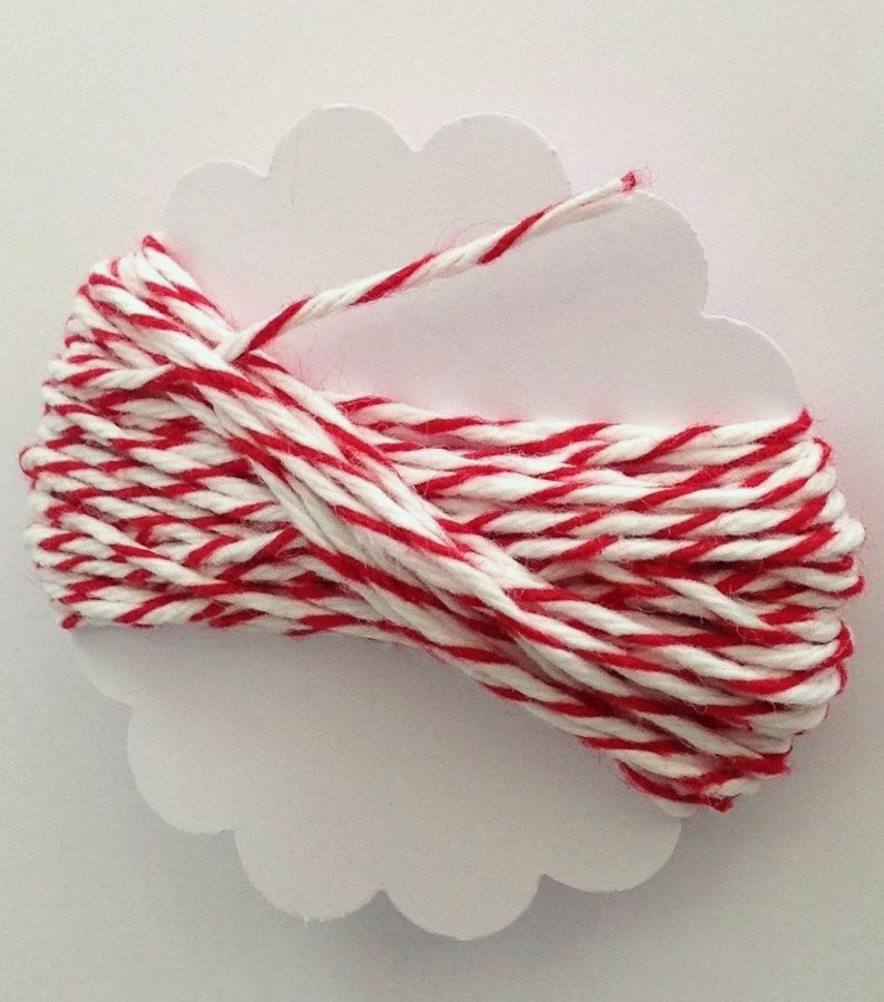 May include: A spool of red and white striped twine is wrapped around a white, cloud-shaped card. The twine is tightly wound, with the red stripes evenly spaced among the white. The card provides a clean, neutral backdrop for the colorful twine.