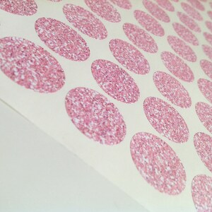 May include: Sheet of stickers with a repeating pattern of pink glitter ovals. The ovals are densely packed with glitter, creating a sparkling effect. The stickers are on a white background.