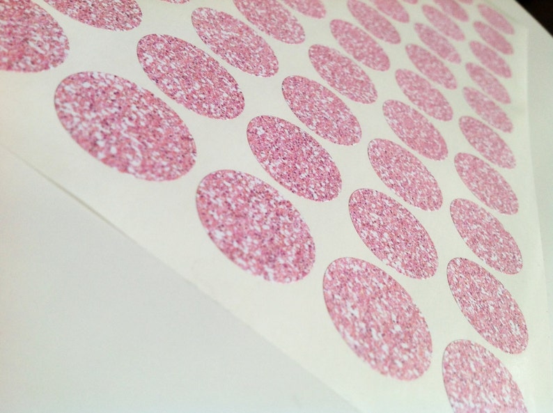 May include: Sheet of stickers with a repeating pattern of pink glitter ovals. The ovals are densely packed with glitter, creating a sparkling effect. The stickers are on a white background.