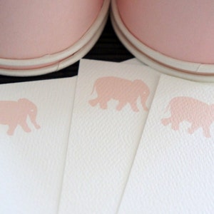 May include: Pink stationery with a light pink elephant design. The stationery is displayed with a pair of pink shoes with white soles. The stationery has a textured surface.