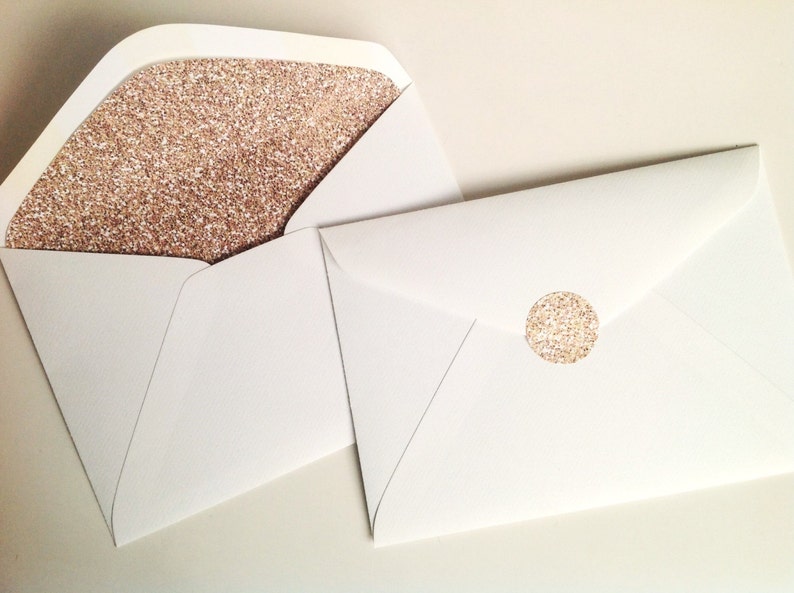 May include: White envelopes, one open to show a rose gold glitter lining, the other sealed with a matching round sticker. The envelopes are suitable for invitations or special announcements. The glitter adds a touch of elegance.