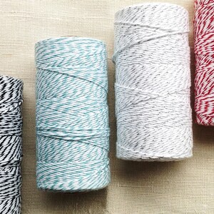 May include: A collection of colorful twine spools. The spools display a variety of colors, including black and white, teal and white, gray and white, and red and white. The twine is tightly wound, creating a textured appearance. Ideal for crafting and gift wrapping.
