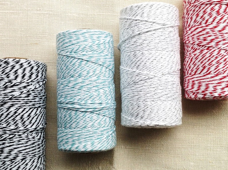 May include: A collection of colorful twine spools. The spools display a variety of colors, including black and white, teal and white, gray and white, and red and white. The twine is tightly wound, creating a textured appearance. Ideal for crafting and gift wrapping.