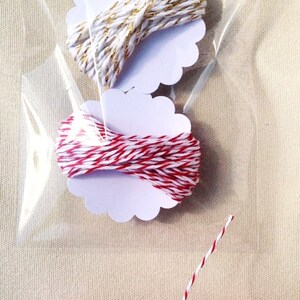 May include: Clear cellophane bag containing two spools of twine on white scalloped tags. One spool is white and gold, the other is red and white. A larger spool of red and white twine is at the bottom.