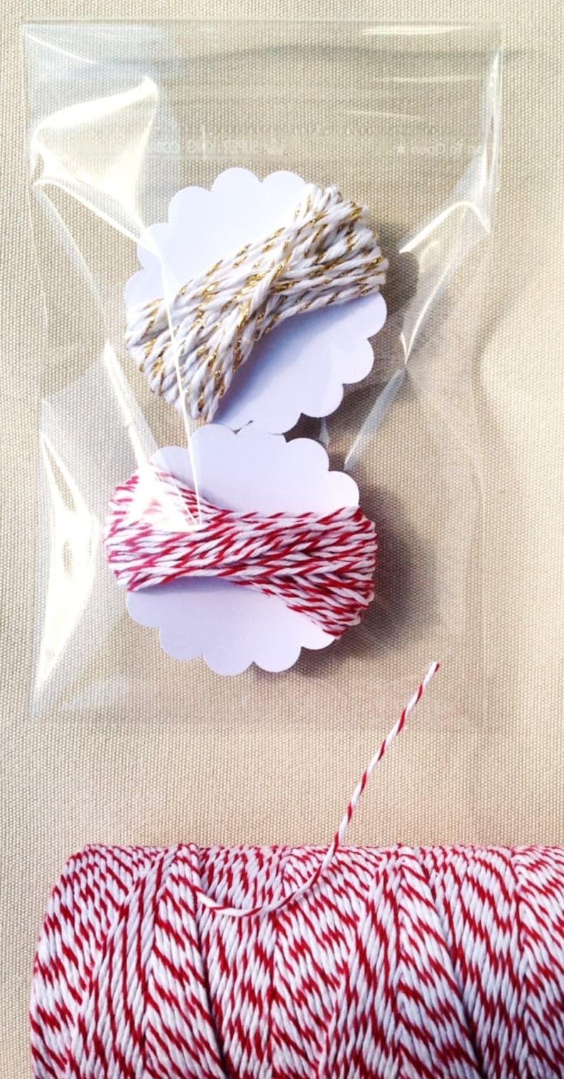 May include: Clear cellophane bag containing two spools of twine on white scalloped tags. One spool is white and gold, the other is red and white. A larger spool of red and white twine is at the bottom.