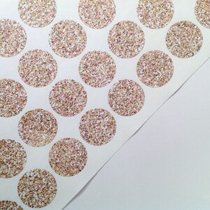 May include: Sheet of circular stickers with a glittery, speckled design in gold, bronze, and white. The stickers are arranged in a grid pattern on a white background, with a corner of the sheet peeled back.