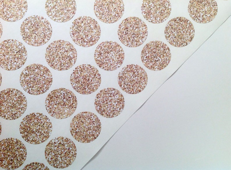 May include: Sheet of circular stickers with a glittery, speckled design in gold, bronze, and white. The stickers are arranged in a grid pattern on a white background, with a corner of the sheet peeled back.