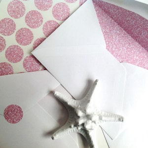 May include: White envelopes with pink glitter accents and a white starfish. Some envelopes have pink glitter polka dots on the inside. One envelope has a pink glitter dot sticker on the front.