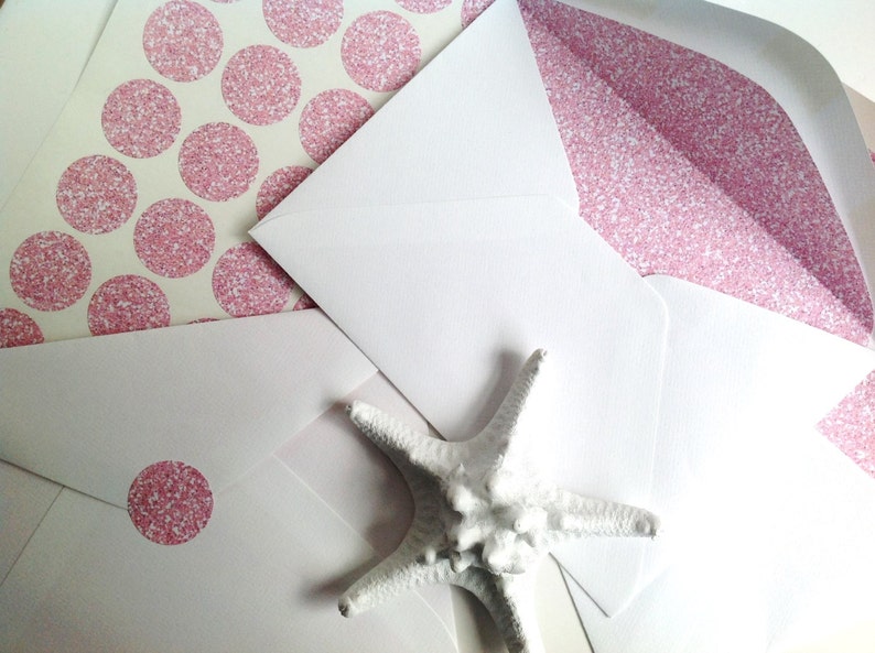 May include: White envelopes with pink glitter accents and a white starfish. Some envelopes have pink glitter polka dots on the inside. One envelope has a pink glitter dot sticker on the front.