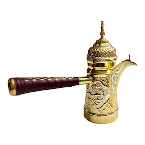 Könnte beinhalten: Eine goldene und silberne Kaffeekanne mit aufwendigen Verzierungen. Die Kanne hat einen Holzgriff und einen Deckel mit einem Knauf.