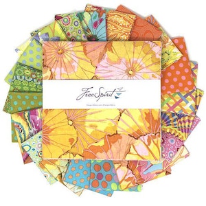 May include: A collection of colorful fabric squares arranged in a circular pattern. The fabrics feature floral and geometric designs in shades of yellow, orange, pink, green, and blue. The center displays a white label with the text "Free Spirit".