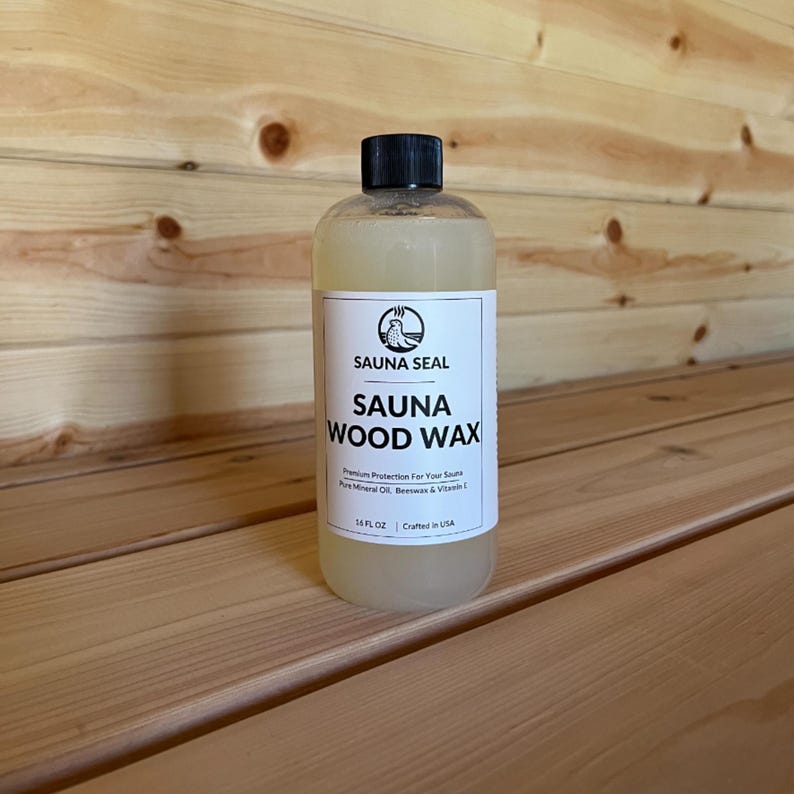 May include: A clear bottle of Sauna Seal Sauna Wood Wax. The bottle is labeled with black text on a white background. The text reads 'Sauna Seal', 'Sauna Wood Wax', 'Premium Protection For Your Sauna', 'Pure Mineral Oil, Beeswax & Vitamin E', '16 FL OZ', and 'Crafted in USA'.