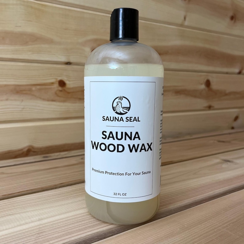 May include: A clear plastic bottle with a black cap, filled with a light yellow liquid. The label reads "SAUNA SEAL SAUNA WOOD WAX" with a logo of a bird. The bottle contains 32 fl oz of product. The background is wooden planks.