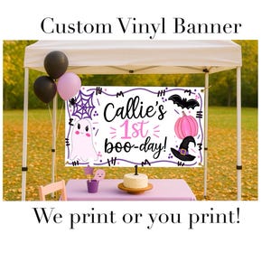 May include: A custom vinyl banner for a first birthday, with the text "Callie's 1st boo-day!" and Halloween-themed graphics. The banner is displayed outdoors with balloons and a small cake on a table. The text "We print or you print!" is also included.