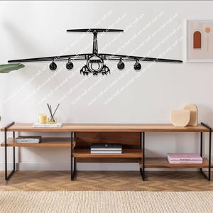 May include: A black metal wall art piece depicting an airplane. The artwork is mounted on a white wall above a wooden console table with black metal legs. A large potted plant and other decorative items are also visible.